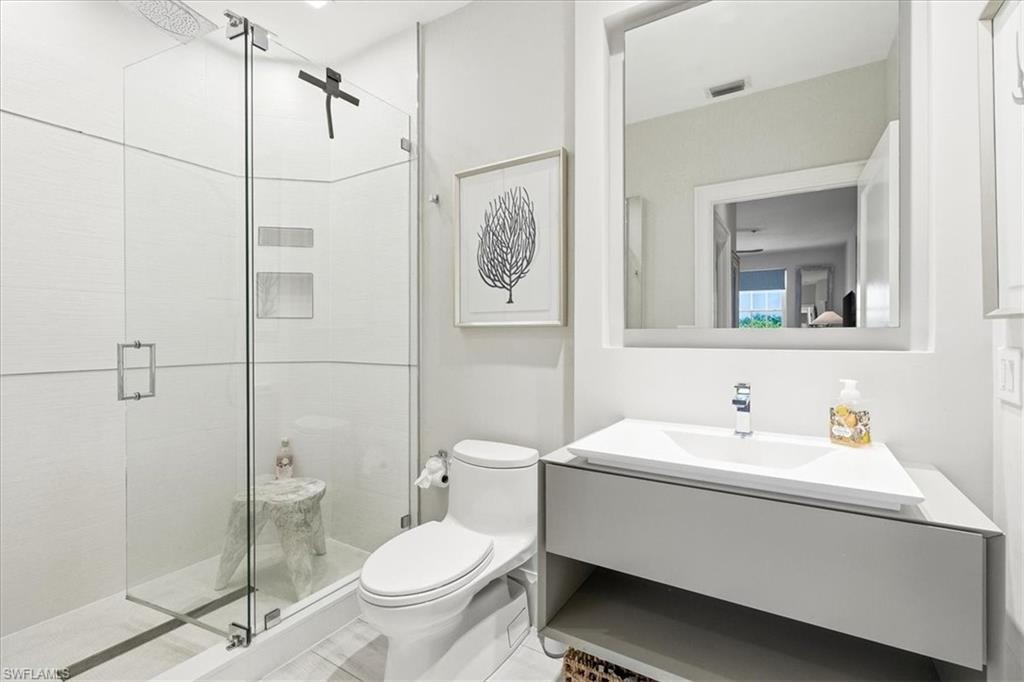 Modern bathroom featuring a frameless glass shower enclosure, a sleek floating vanity with an integrated sink, a contemporary wall-mounted mirror, and a white toilet