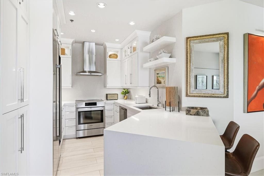 Contemporary kitchen featuring white cabinetry, stainless steel appliances, a range hood, and a white countertop with an integrated sink