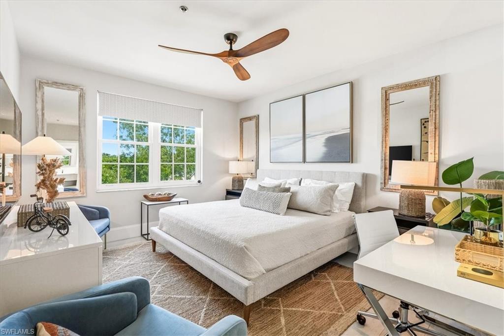 Light-filled sleeping area featuring a wood-finish ceiling fan, broad window, and light-toned walls