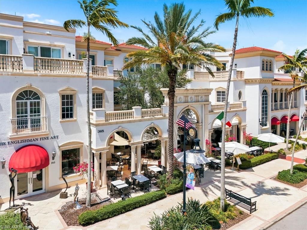 Mediterranean-inspired building featuring stucco exterior, red tile roofing, decorative balustrades, arched entryways, and prominent palm trees