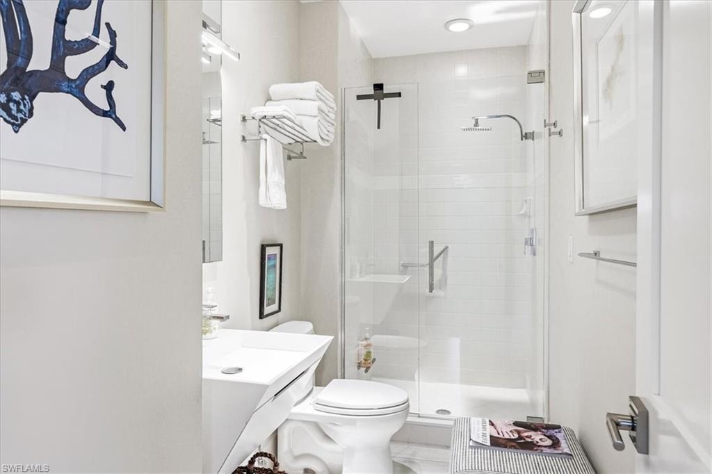 Modern bathroom featuring a glass-enclosed shower with subway tile surround, a wall-mounted vanity with an integrated sink, a recessed ceiling light, and a toilet