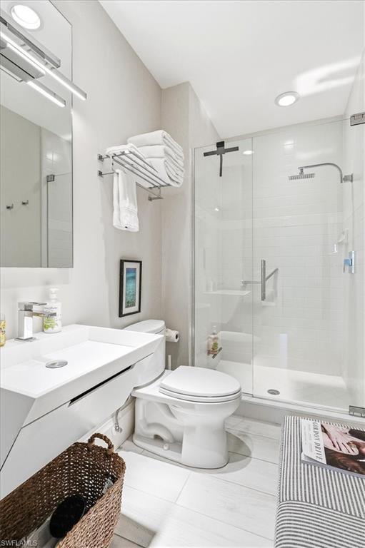 Contemporary bathroom featuring a floating vanity with an integrated sink, a glass-enclosed shower with a rainfall showerhead, and light-toned tile flooring