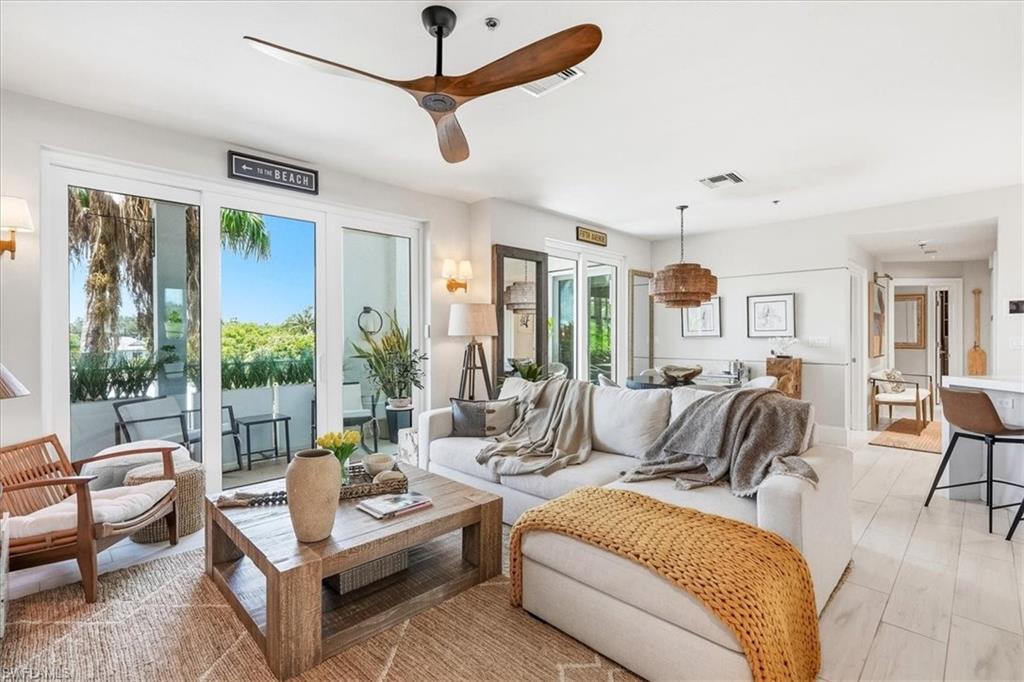 Living space featuring light-toned flooring, a wood-finish ceiling fan, and sliding glass doors opening to an outdoor patio with black metal railings