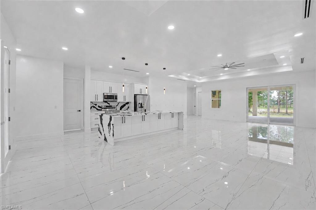 Open-concept living area featuring large format porcelain tile flooring, a kitchen island with a waterfall countertop, recessed lighting, and a tray ceiling with a ceiling fan