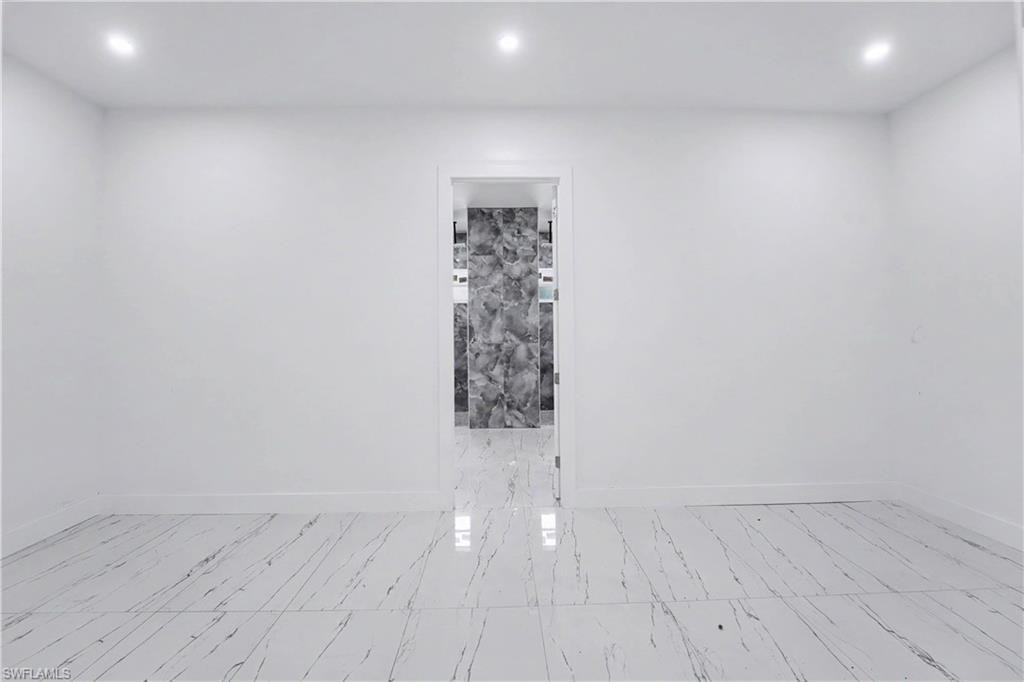 Spacious room featuring white walls, recessed ceiling lighting, and large format white tile flooring with dark veining