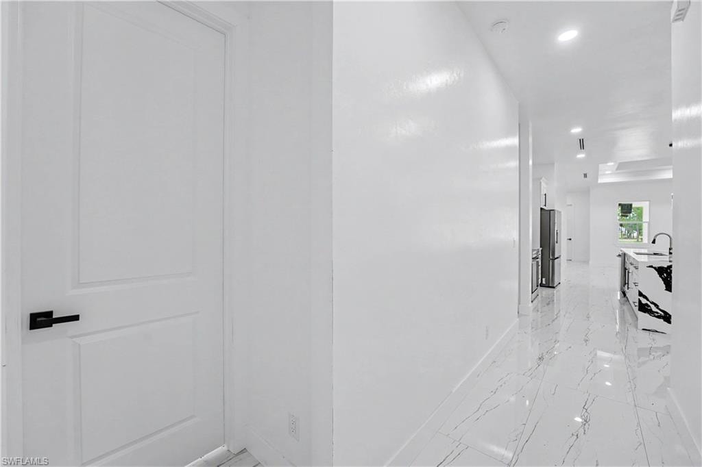 Hallway featuring white walls, recessed lighting, and large format white tile flooring with dark veining