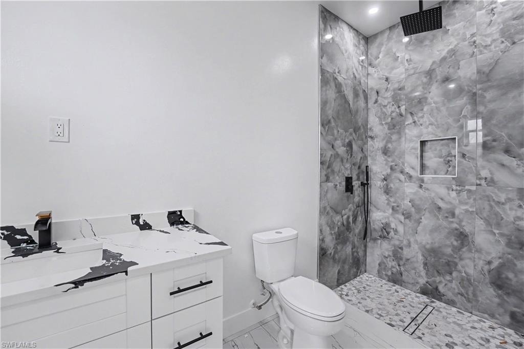 Spacious shower featuring floor-to-ceiling marbled gray tile, a recessed niche, and a linear drain