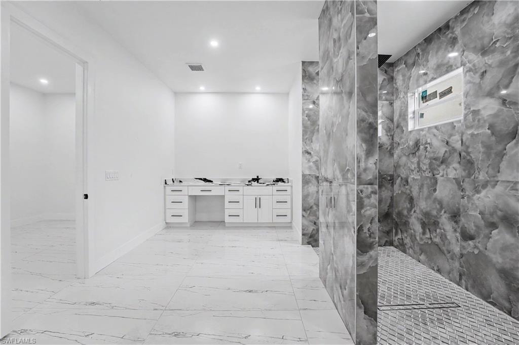 Spacious bathroom featuring large format marble-look floor tiles, a white double vanity with multiple drawers, and a walk-in shower with natural stone-look wall tiles and a mosaic tile floor