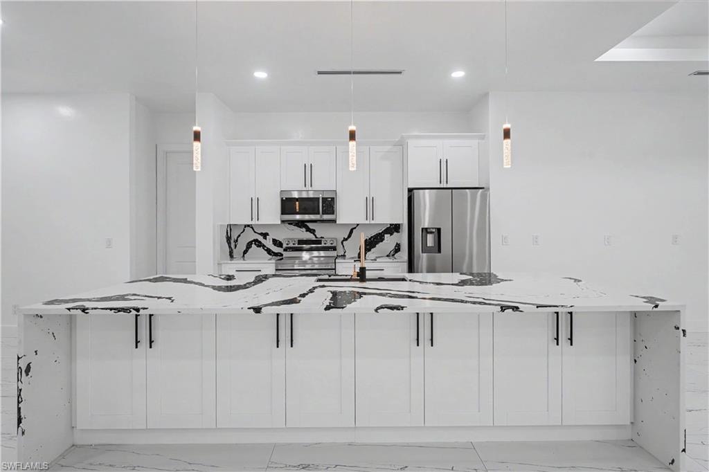 Modern kitchen featuring an expansive island with a waterfall countertop, white cabinetry, integrated stainless steel appliances, a striking black and white backsplash, and contemporary pendant lighting