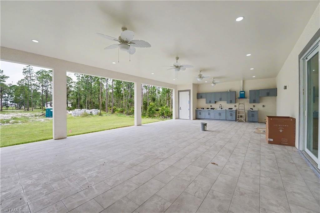 Expansive covered patio featuring large format tile flooring, an outdoor kitchen with cabinetry and sink, multiple ceiling fans, recessed lighting, and a sliding glass door entry