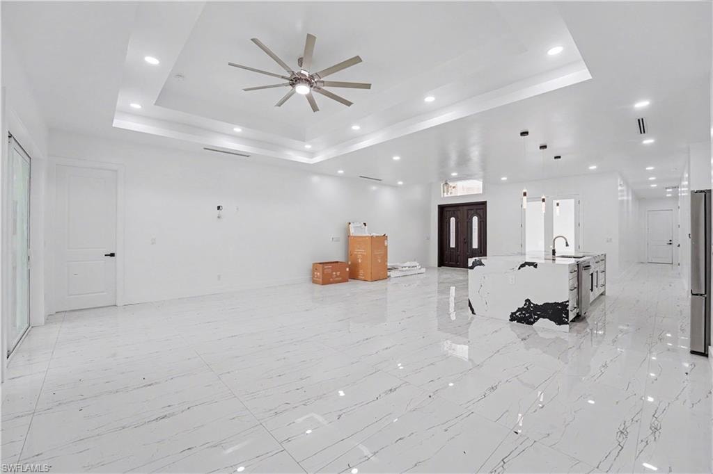 Open-concept living space featuring high ceilings with tray detailing and recessed lighting, large format polished tile flooring, and a contemporary ceiling fan