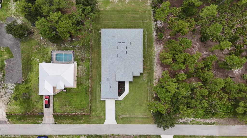 Property featuring a light gray roof, an expansive concrete driveway, and surrounding green lawn