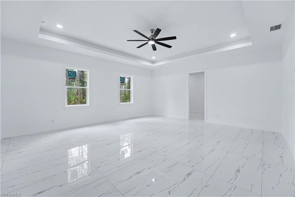 Spacious room featuring white walls, large format tile flooring, and a tray ceiling with recessed lighting