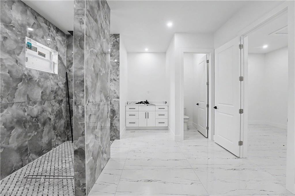 Spacious bathroom featuring large format marble-look floor tiling, a walk-in shower with stone-patterned wall tiles and mosaic floor tiling, and a white vanity with integrated cabinetry