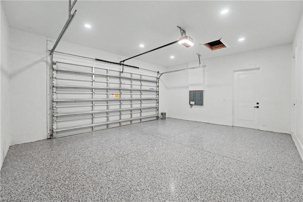 Spacious garage featuring epoxy flooring, overhead door with automatic opener, recessed lighting, and a paneled interior door