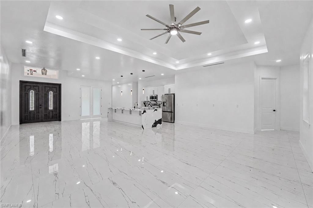 Expansive open-concept interior featuring large format marble-look tile flooring, a tray ceiling with recessed lighting, and a modern ceiling fan
