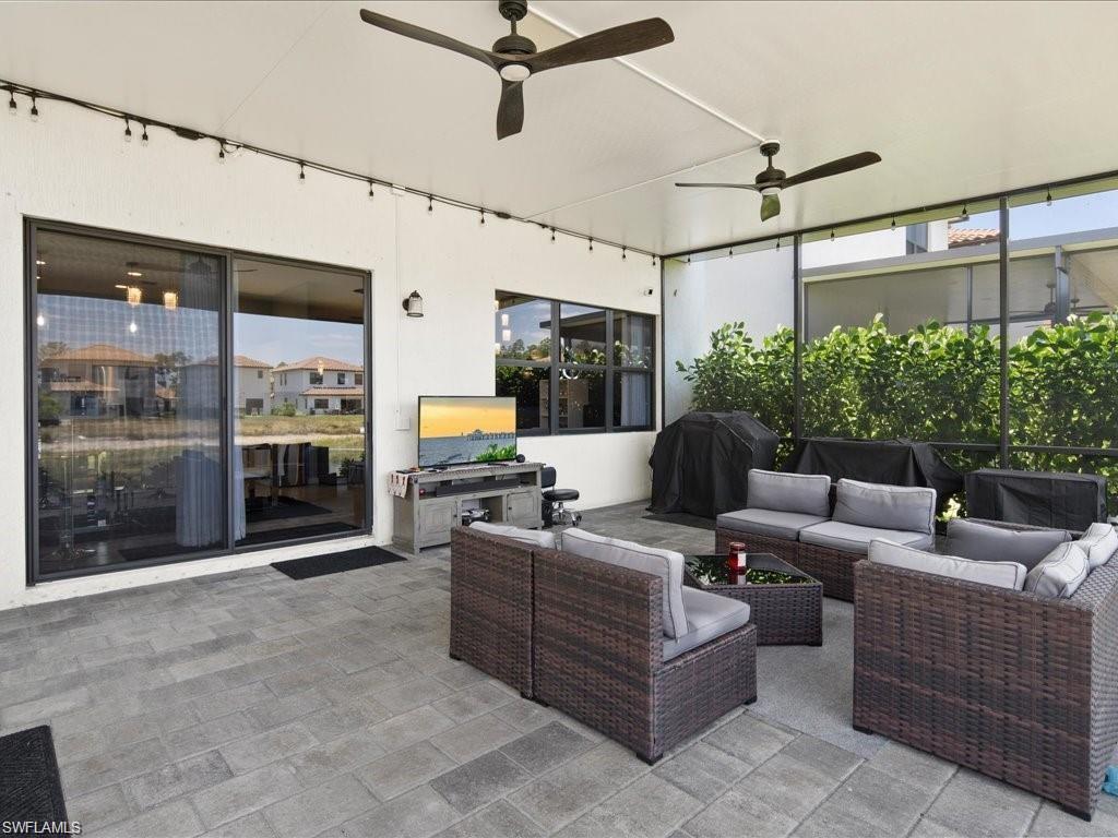 Expansive covered patio featuring a paver floor, two ceiling fans, string lighting, and direct access to the interior via sliding glass doors