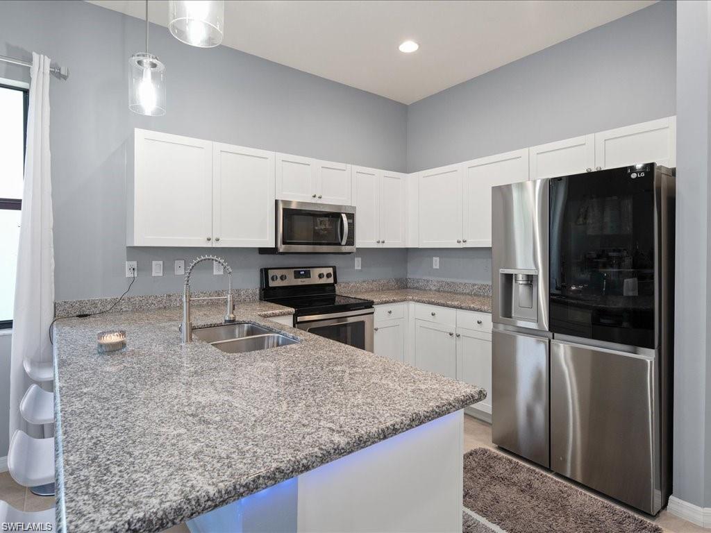 Kitchen featuring white shaker-style cabinetry, a stainless steel appliance suite, speckled stone countertops, and a double basin stainless steel sink with a gooseneck faucet