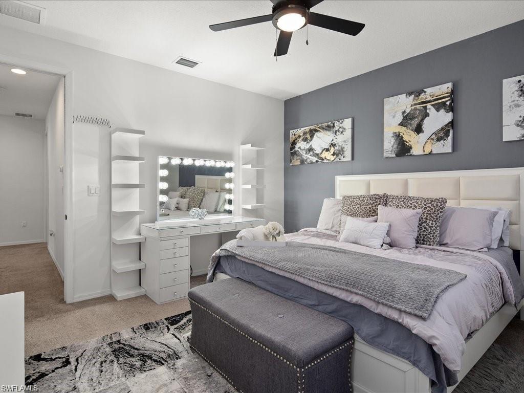Bedroom featuring a padded headboard, a ceiling fan with integrated lighting, and a built-in vanity with illuminated mirror