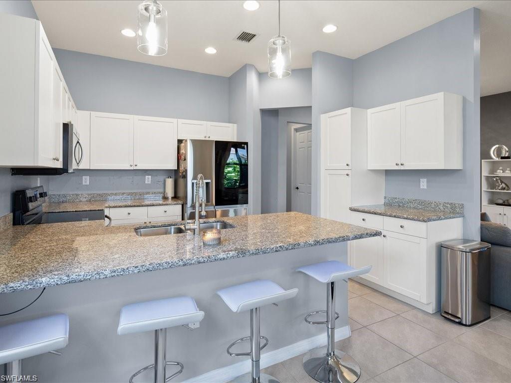 Modern kitchen featuring a breakfast bar with seating, light granite countertops, white cabinetry, a double basin undermount sink with a gooseneck faucet, and recessed and pendant lighting