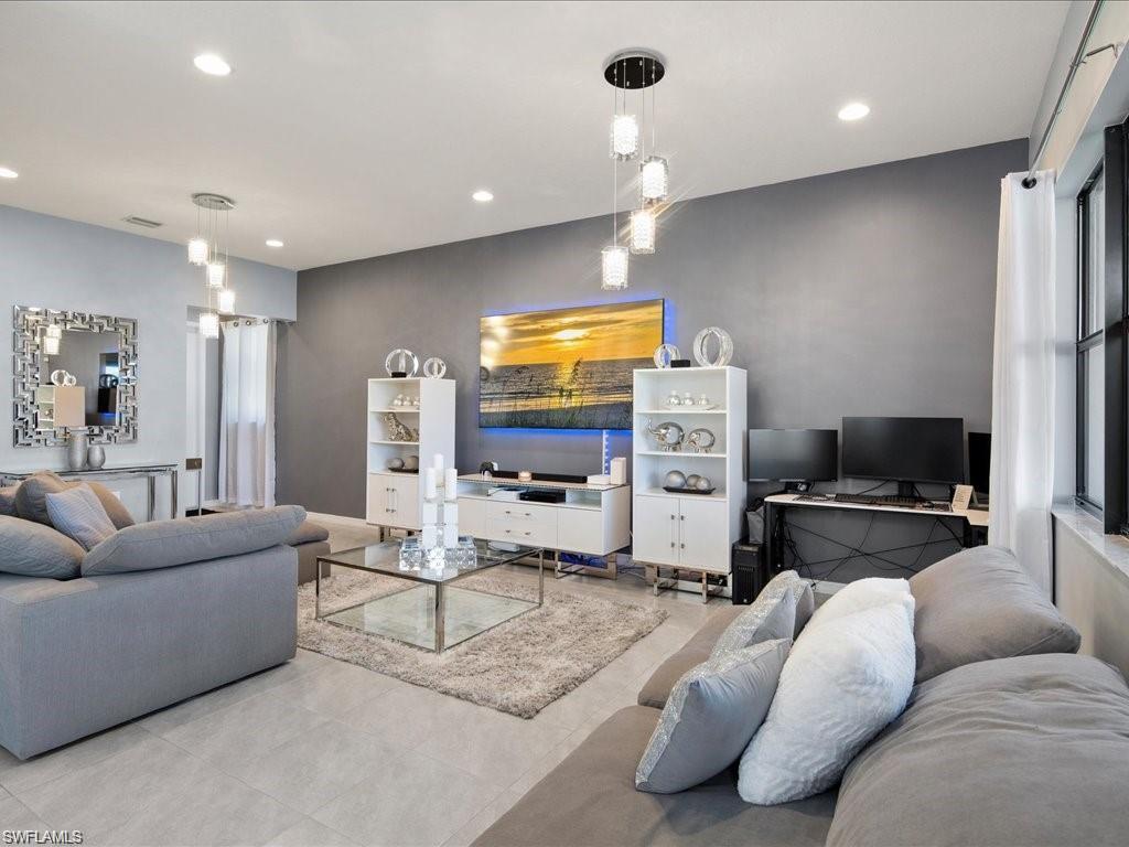 Spacious living area featuring light-toned tile flooring, recessed lighting, and a contemporary multi-light pendant fixture