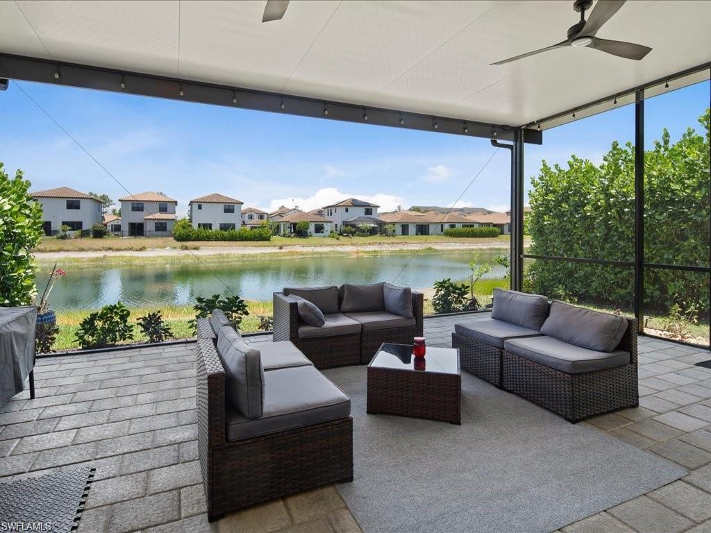 Screened-in covered patio featuring a paver floor, water view, ceiling fan, and string lighting