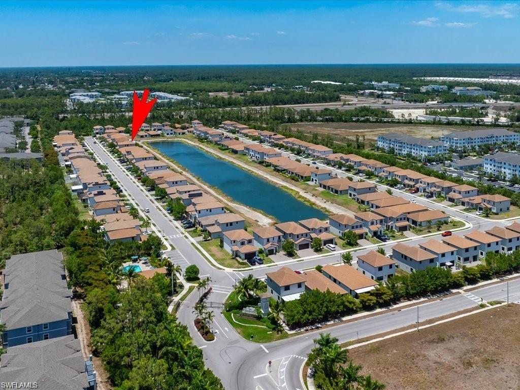 Aerial view of a residential community featuring a prominent central water feature, uniform architectural styles, paved roadways, and surrounding natural landscapes
