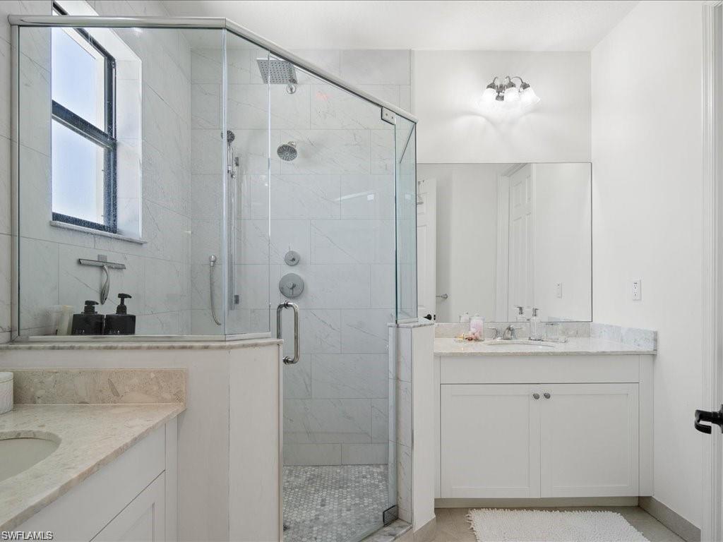 Glass-enclosed shower with multiple shower heads and a window, complemented by a white vanity with a light-colored countertop