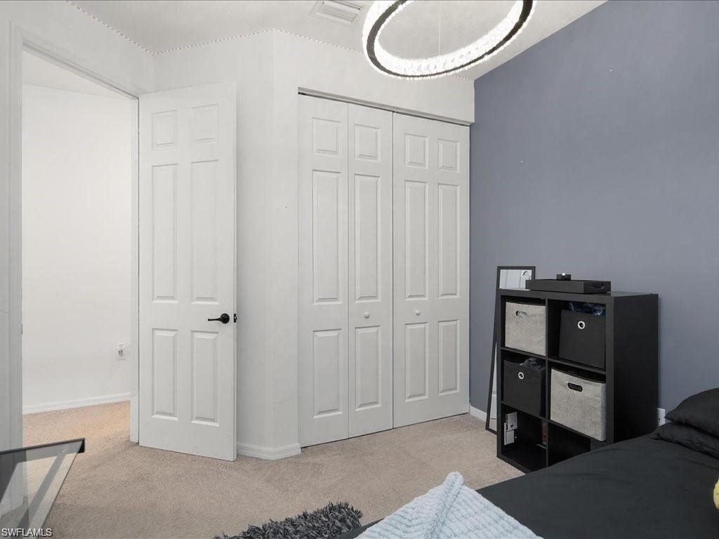 Bedroom featuring light neutral carpet, a contemporary circular ceiling light fixture, and two sets of bifold panel doors