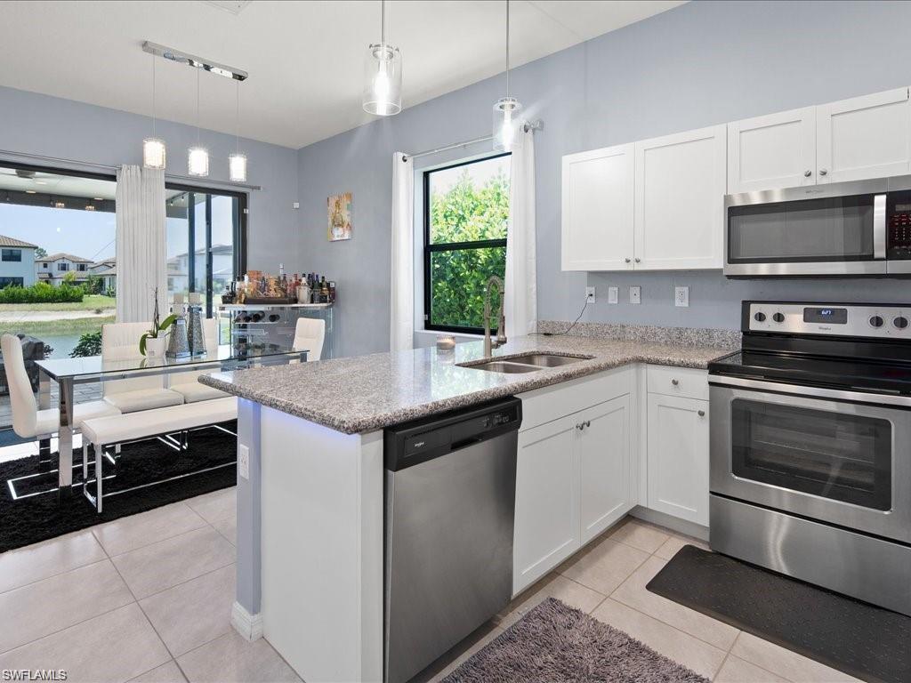 Open-concept kitchen featuring white cabinetry, stainless steel appliances, granite countertops, and an integrated dining area with sliding glass doors