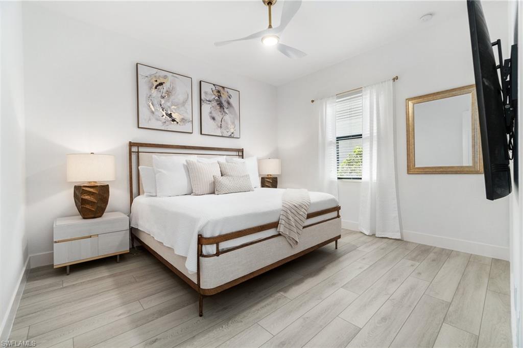 Bright interior space featuring light wood-finish flooring, a ceiling fan with integrated lighting, and a single window with blinds and sheer curtains