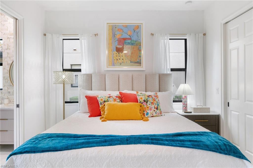 Bedroom featuring a paneled upholstered headboard, dual windows with white drapery, and a six-panel door