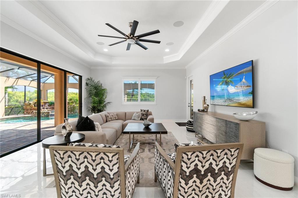 Spacious living area featuring white tile flooring, tray ceilings with recessed lighting, and a contemporary ceiling fan