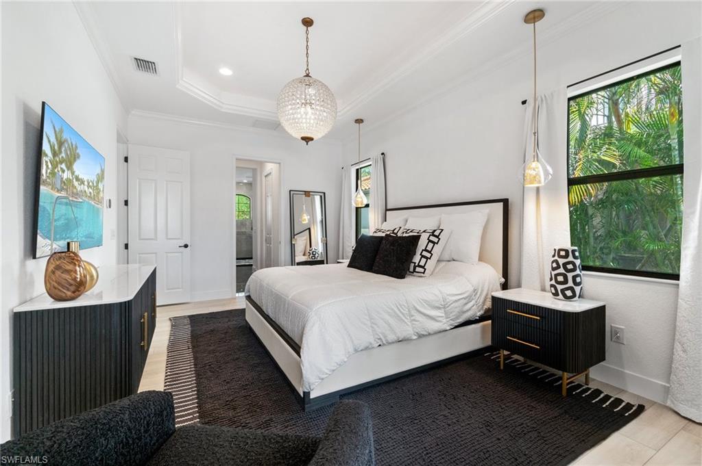 Spacious bedroom featuring a tray ceiling, a central chandelier, and recessed lighting