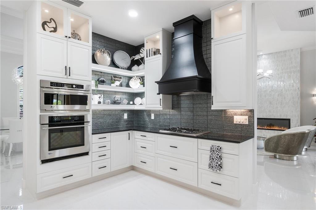 Contemporary kitchen featuring white cabinetry, a black range hood, stainless steel appliances, dark countertops, and a textured backsplash