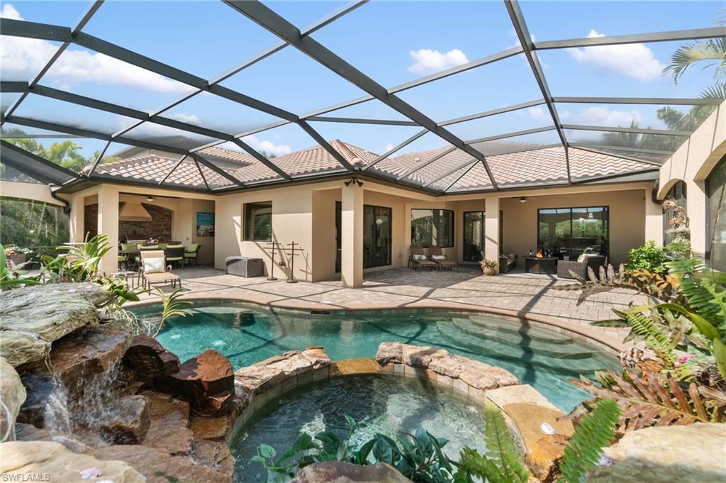 Screened-in outdoor living space featuring a freeform swimming pool with rock waterfall, integrated spa, and extensive paver decking
