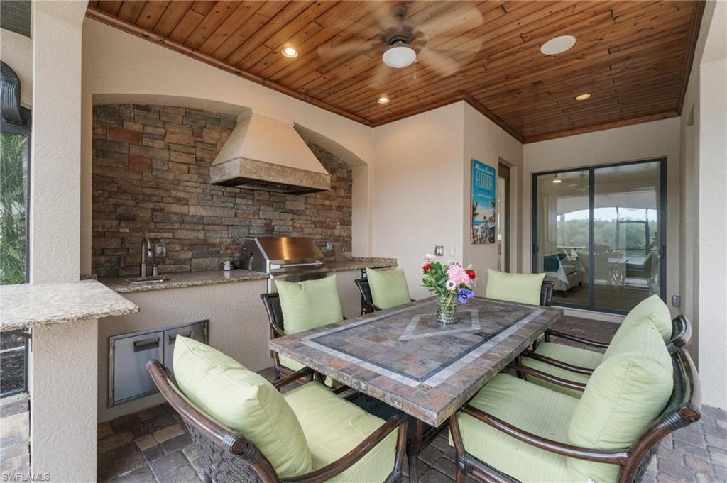 Outdoor kitchen featuring stone veneer backsplash, granite countertops, stainless steel grill, and built-in sink