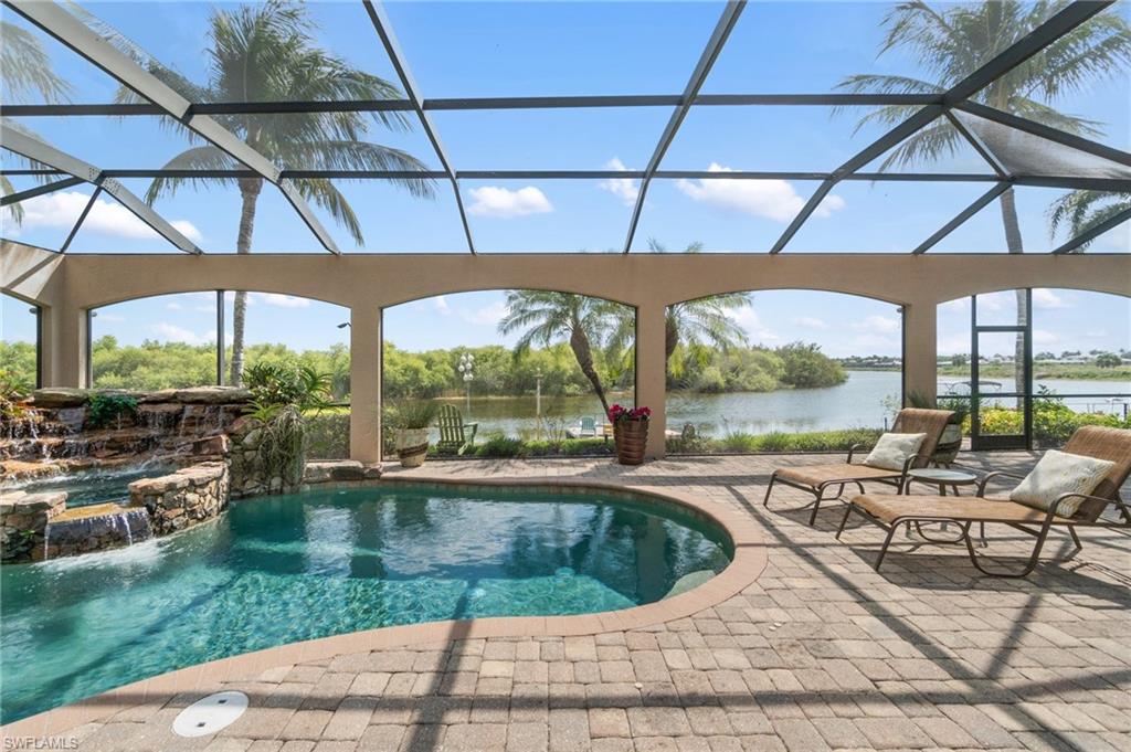 Screened outdoor living area featuring a pool with a rock waterfall, a spa, and paver decking