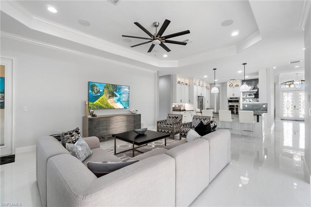 Open-concept living space featuring high-gloss flooring, tray ceilings with recessed lighting, and a modern ceiling fan