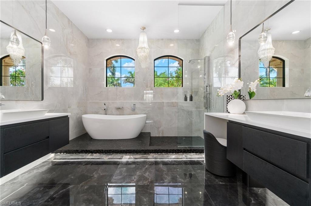 Contemporary bathroom featuring a freestanding tub, dual floating vanities with vessel sinks, a glass-enclosed shower, and arched windows