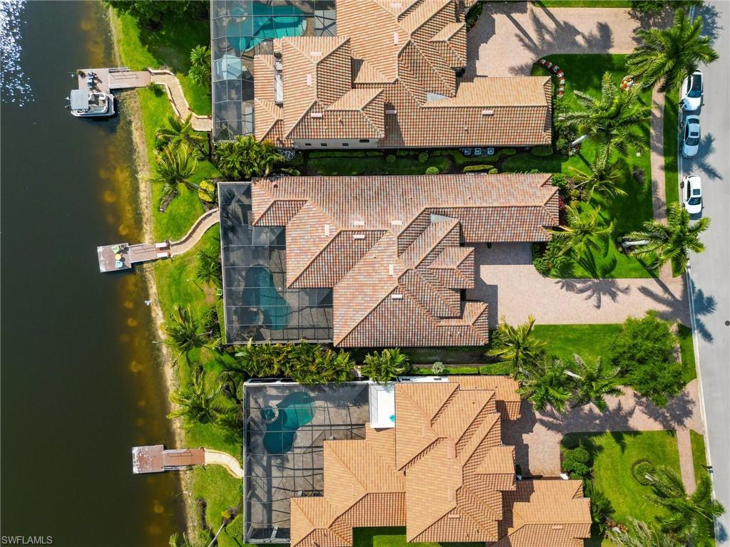 Waterfront property featuring a private boat dock, screened-in swimming pool, paved driveway, and mature landscaping