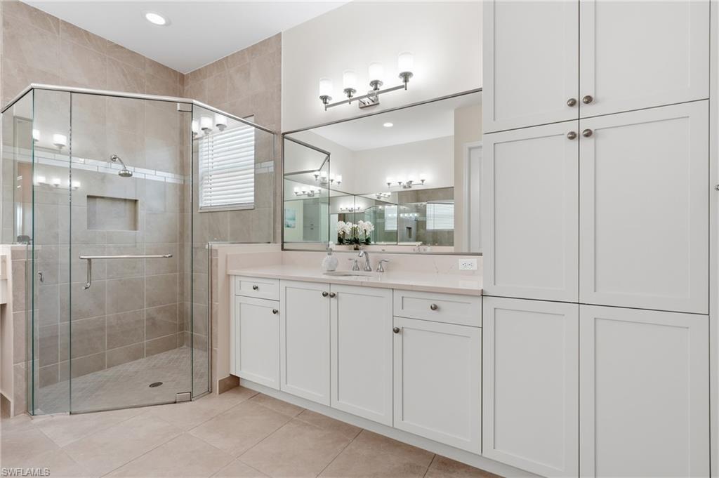 Primary bathroom features a designer glass-enclosed shower, dual vanity with quartz countertops, large format tile flooring.