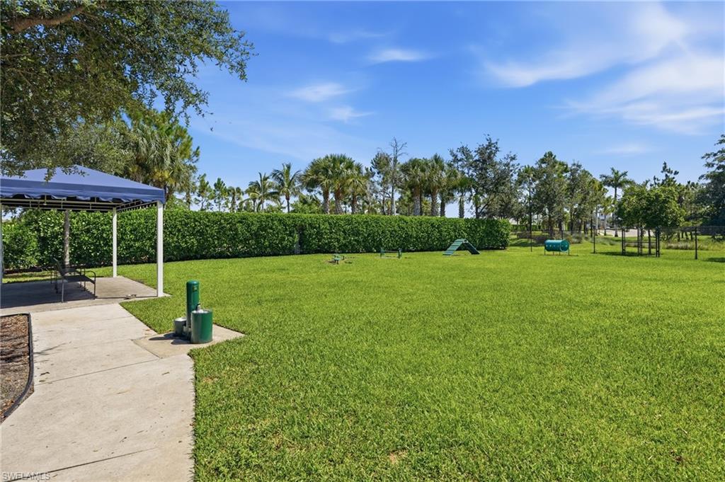 Dog Park 1 of 2 - featuring a shaded pavilion with seating, mature landscaping, paved pathways, and recreational elements for exercise.