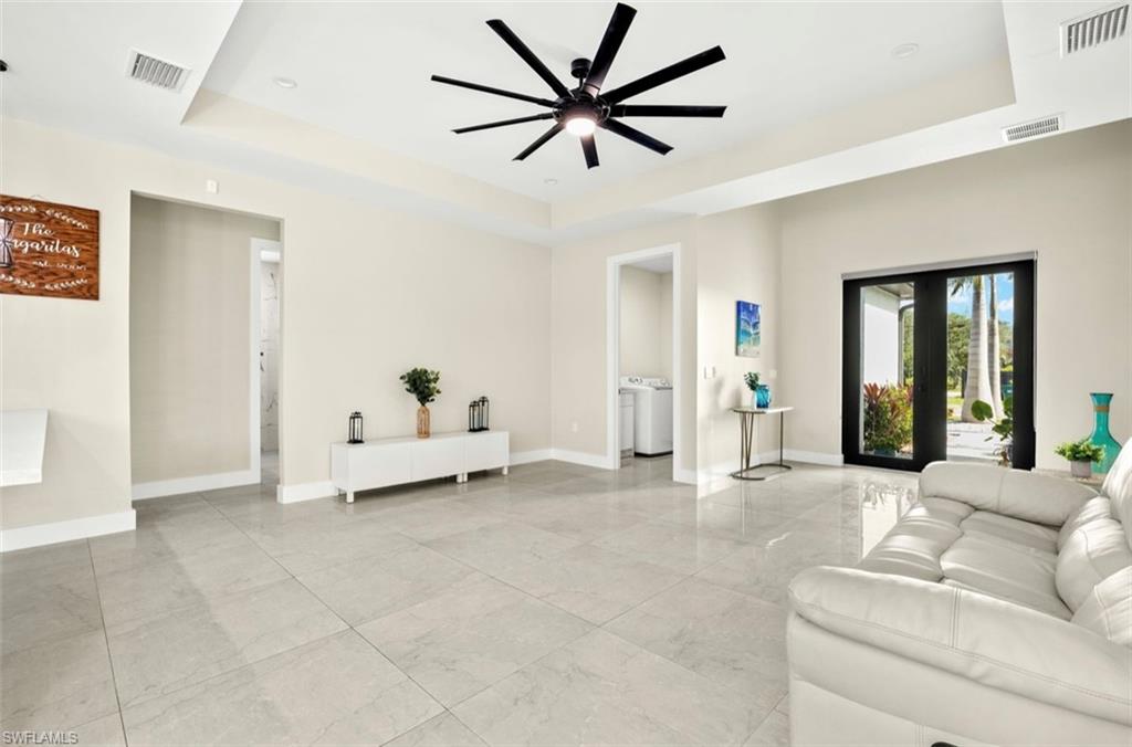 Spacious room featuring light-toned walls, a tray ceiling with a ceiling fan, and large format tile flooring