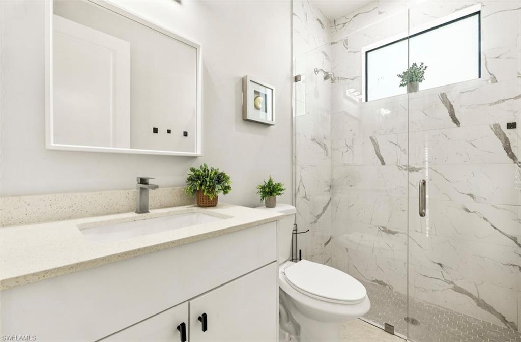 Modern bathroom featuring a quartz vanity countertop with an integrated rectangular sink, a frameless shower with marble-look tile walls, and a glass enclosure