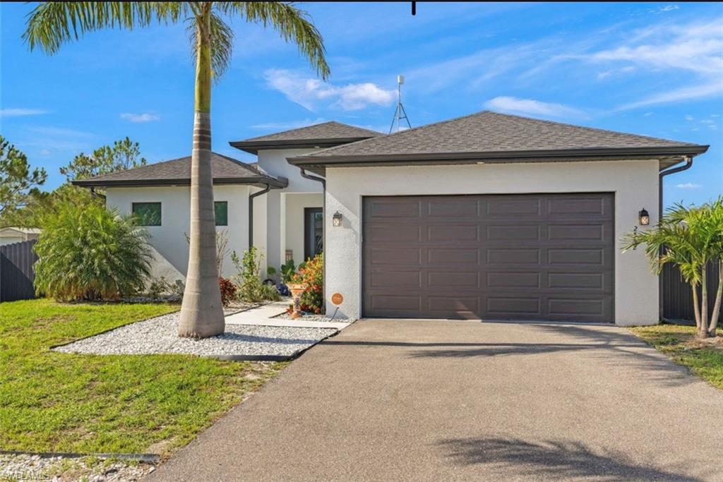 Contemporary stucco exterior with a dark panel garage door, a concrete driveway, and a white gravel landscaping feature