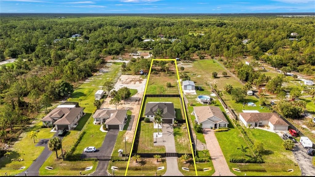 Property aerial showcasing a residential home with a manicured lawn, paved driveway, and established landscaping