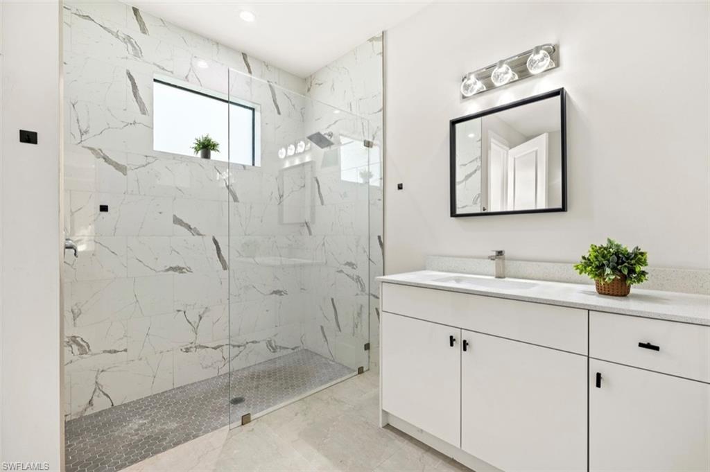 Contemporary bathroom featuring a spacious glass-enclosed shower with large format marble-look tile walls and hexagonal floor tiling