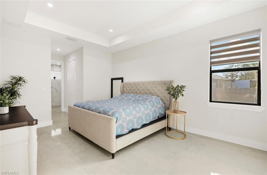 Bright bedroom featuring a tray ceiling with recessed lighting, large window with horizontal blinds, and light-toned tile flooring