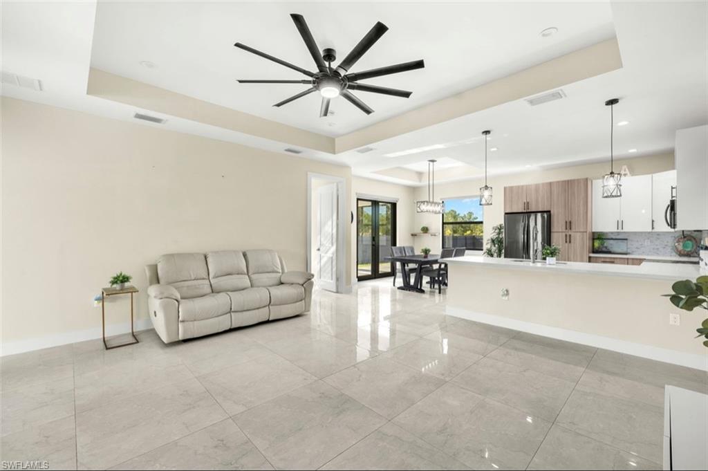 Open-concept living area with large format tile flooring, a tray ceiling, and a contemporary ceiling fan